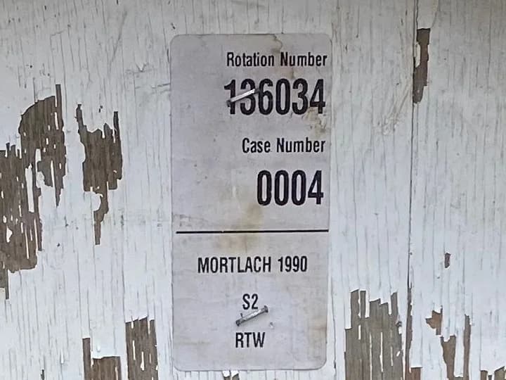 A warehouse rotation-number label stapled to the end of a Mortlach 1990 cask